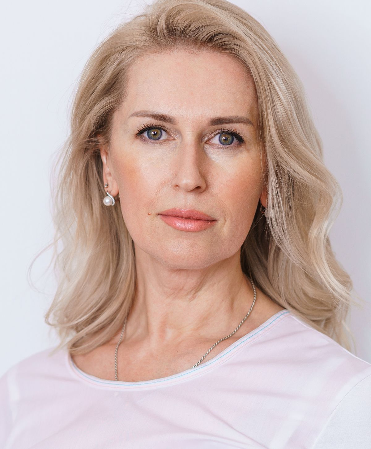 Woman with blonde hair and earrings, neutral expression.
